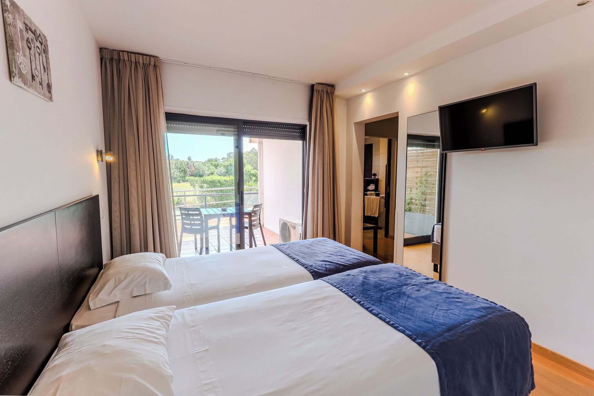 Une chambre d’hôtel avec deux lits, un balcon, une télévision et une vue sur la verdure.