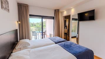 Une chambre d’hôtel avec deux lits, un balcon, une télévision et une vue sur la verdure.