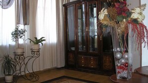 A room with a large wooden cabinet, a potted plant on a metal stand, and a vase with flowers on a table. - Hotel Volter (Lviv)