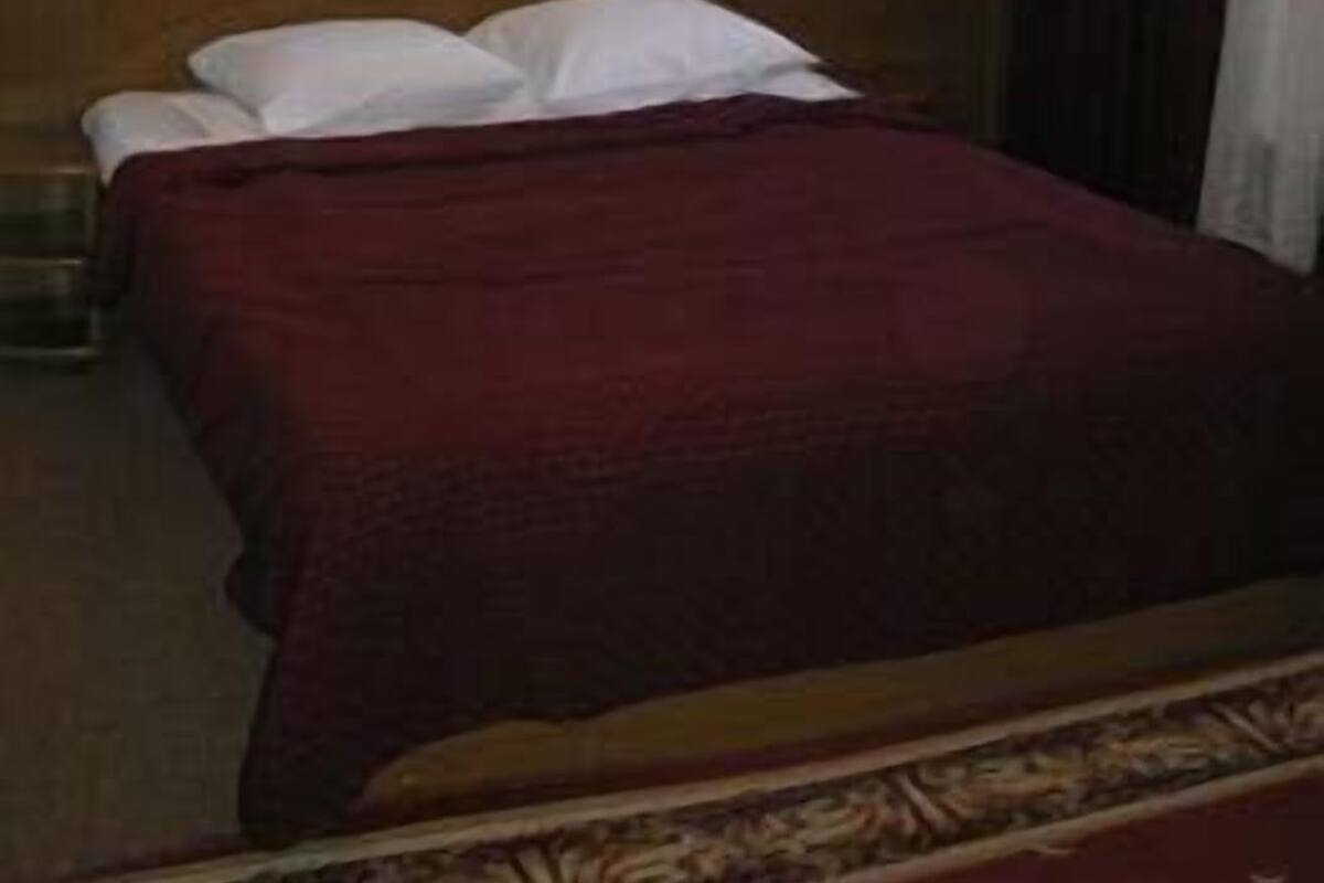 Habitación de hotel con cabecera de madera, cama con almohadas blancas, colcha roja, un cuadro en la pared y una ventana con cortinas.