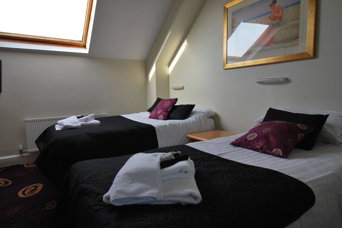 A hotel room with two beds, each with black and white bedding, a small wooden nightstand, and a window with a view of the outside.