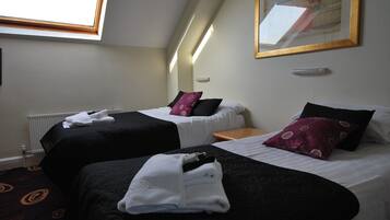 Une chambre d’hôtel avec deux lits, chacun doté de draps noirs et blancs, une petite table de chevet en bois et une fenêtre donnant sur l’extérieur.