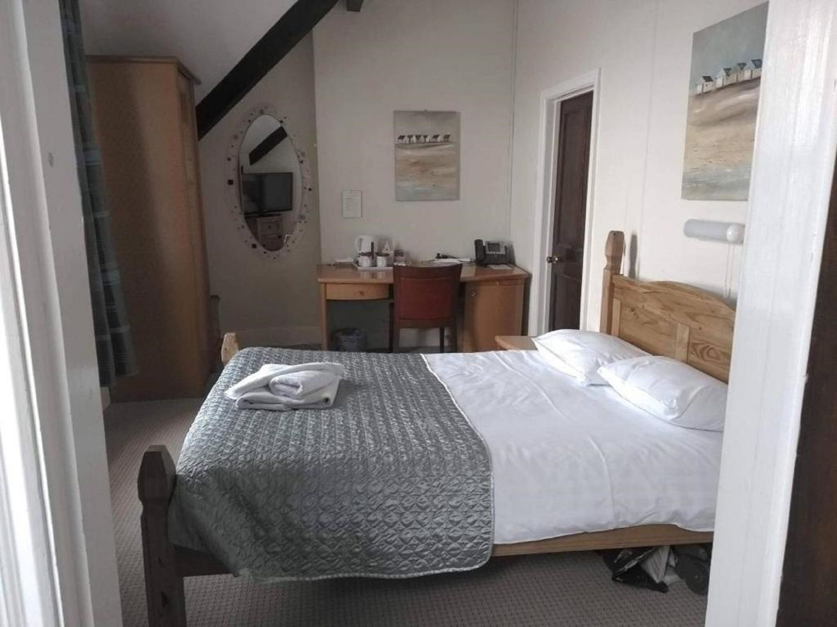 Una habitación de hotel con cama, escritorio, silla, armario y espejo.