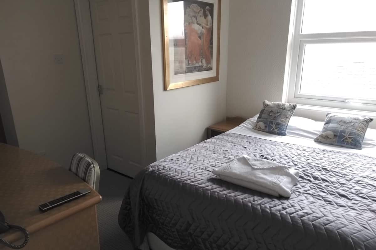 A bedroom with a bed, bedside tables, a desk, and a framed picture on the wall.