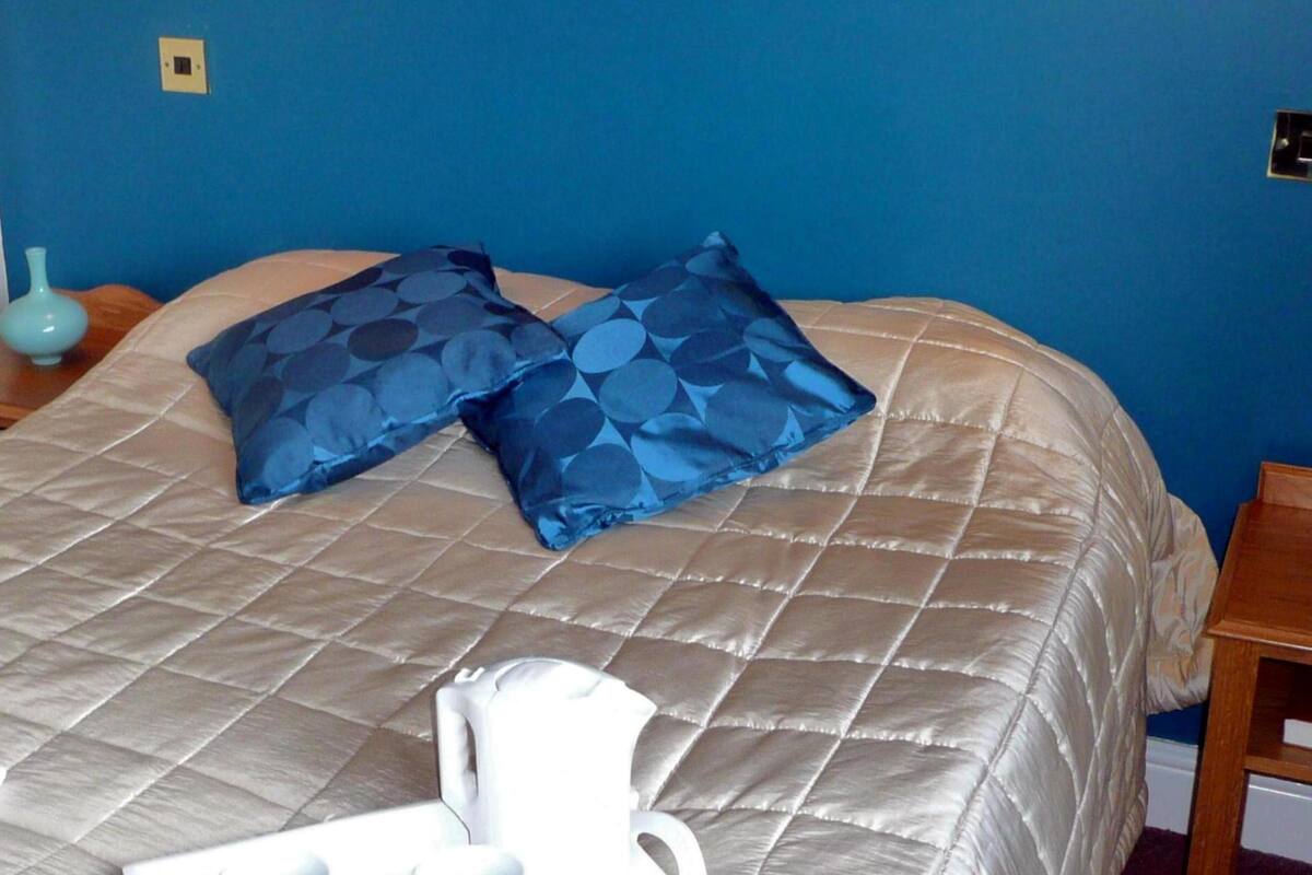 A bed with a beige quilted bedspread and two blue pillows with a circular pattern.