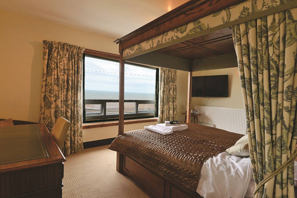 A four-poster bed with a view of the sea, a desk, and a flat-screen TV.