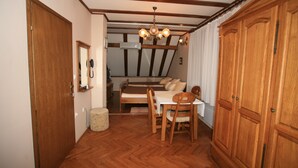 Een kamer met een houten vloer, een eettafel met stoelen, een bed met kussens, een houten kledingkast en een kroonluchter.