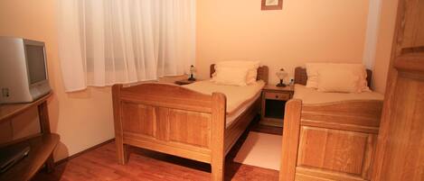 A room with two wooden beds, a desk with a computer, and a window with sheer curtains.