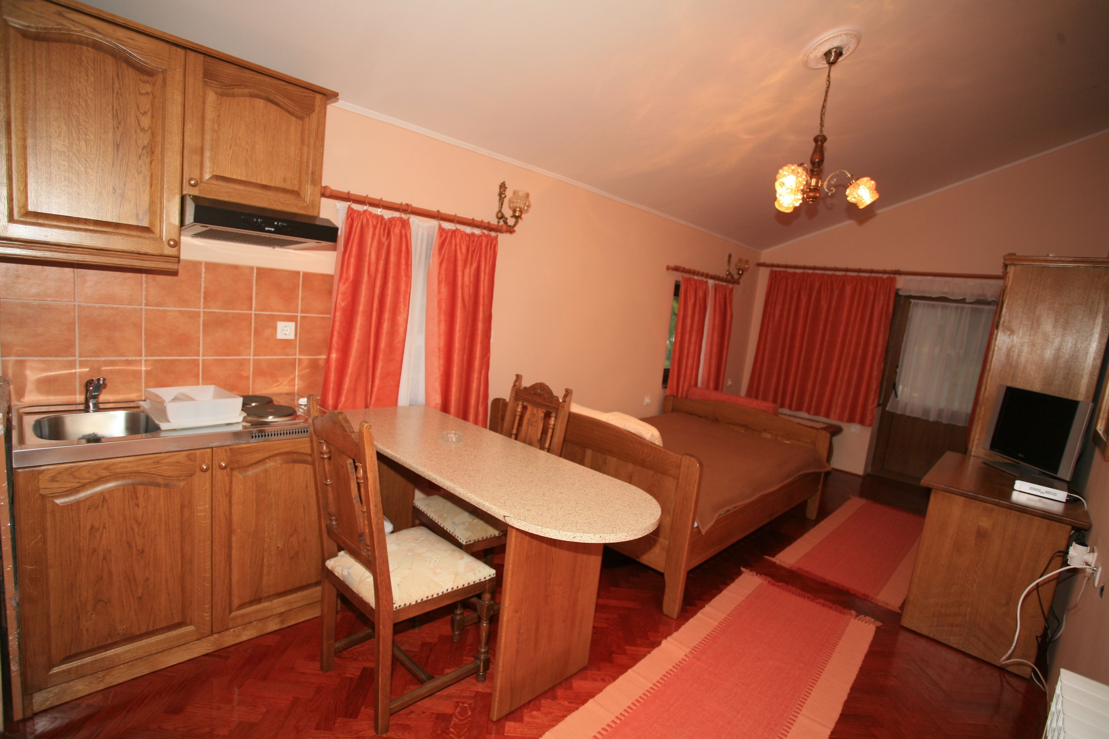 A compact kitchen with wooden cabinets, a dining table, chairs, and a small television.