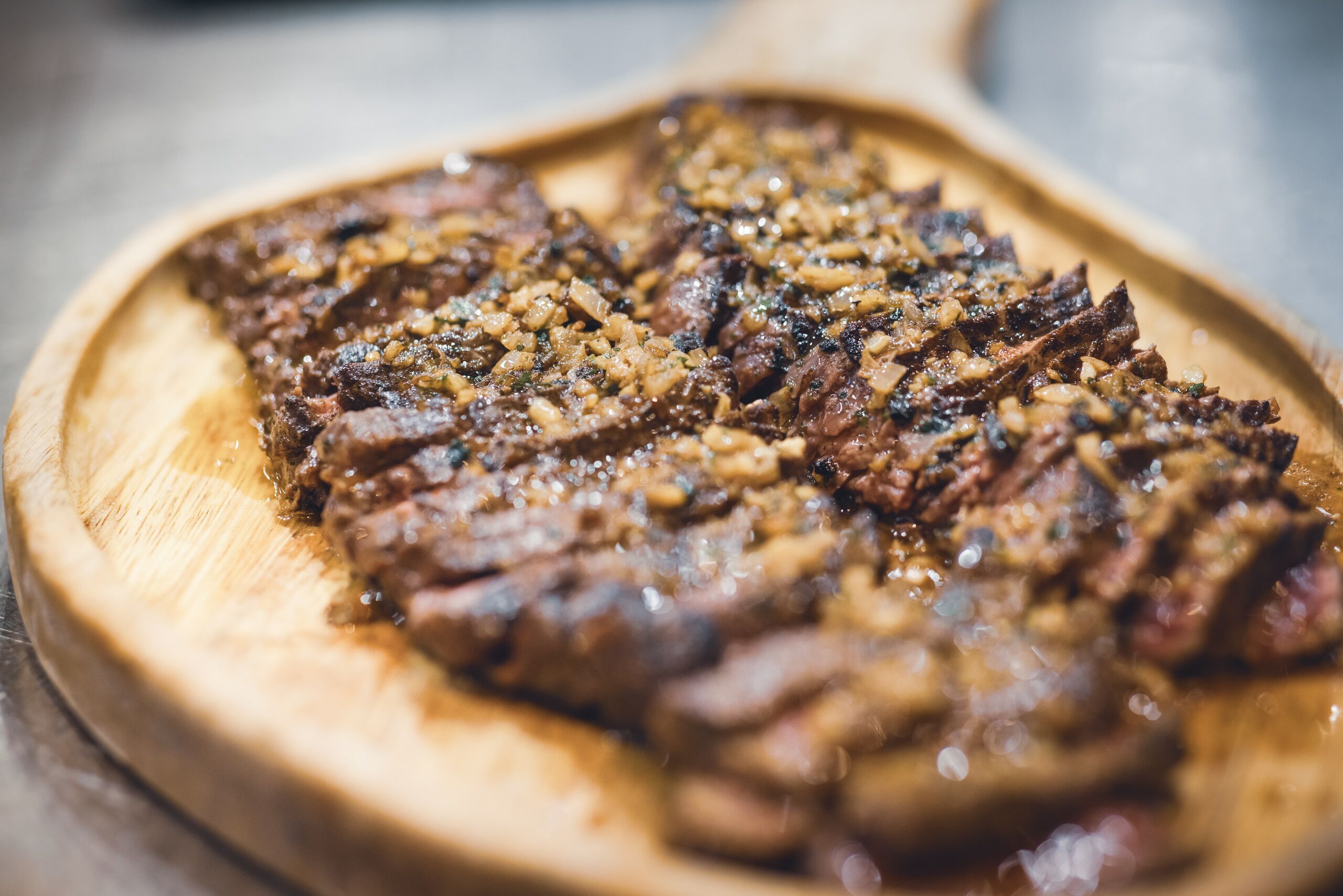 Une planche à découper en bois sur laquelle on a disposé des tranches de viande, probablement du steak, assaisonnées avec des herbes et des épices.