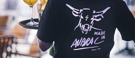 Une personne portant un t-shirt noir orné d’un motif graphique et d’un texte dans le dos, tenant un plateau rempli de boissons.