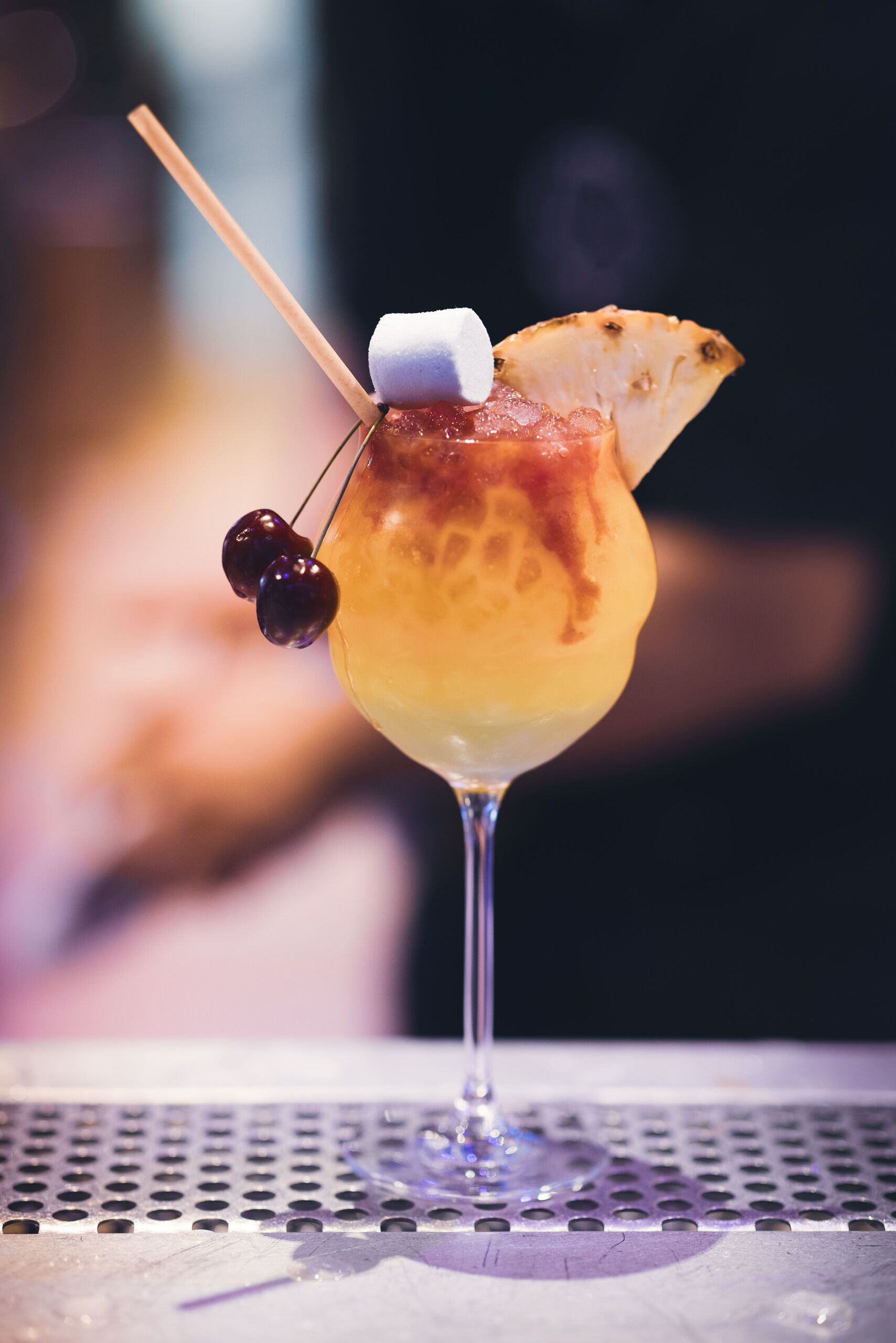 A cocktail with a fruit garnish and a marshmallow on a cocktail glass.