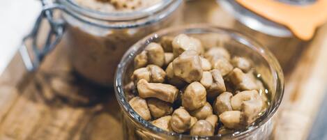 A wooden cutting board with two glass jars containing food items and a bowl of nuts.