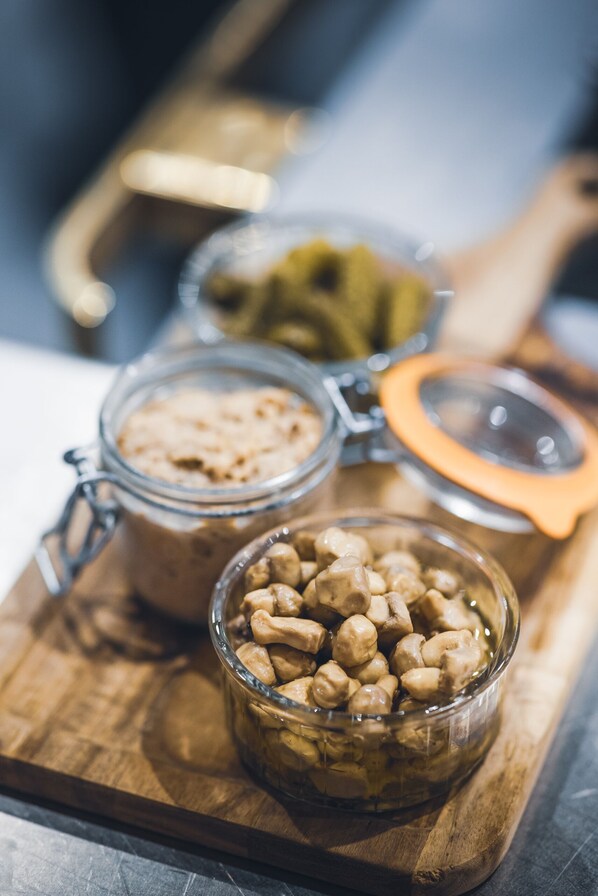 A wooden cutting board with two glass jars containing food items and a bowl of nuts.