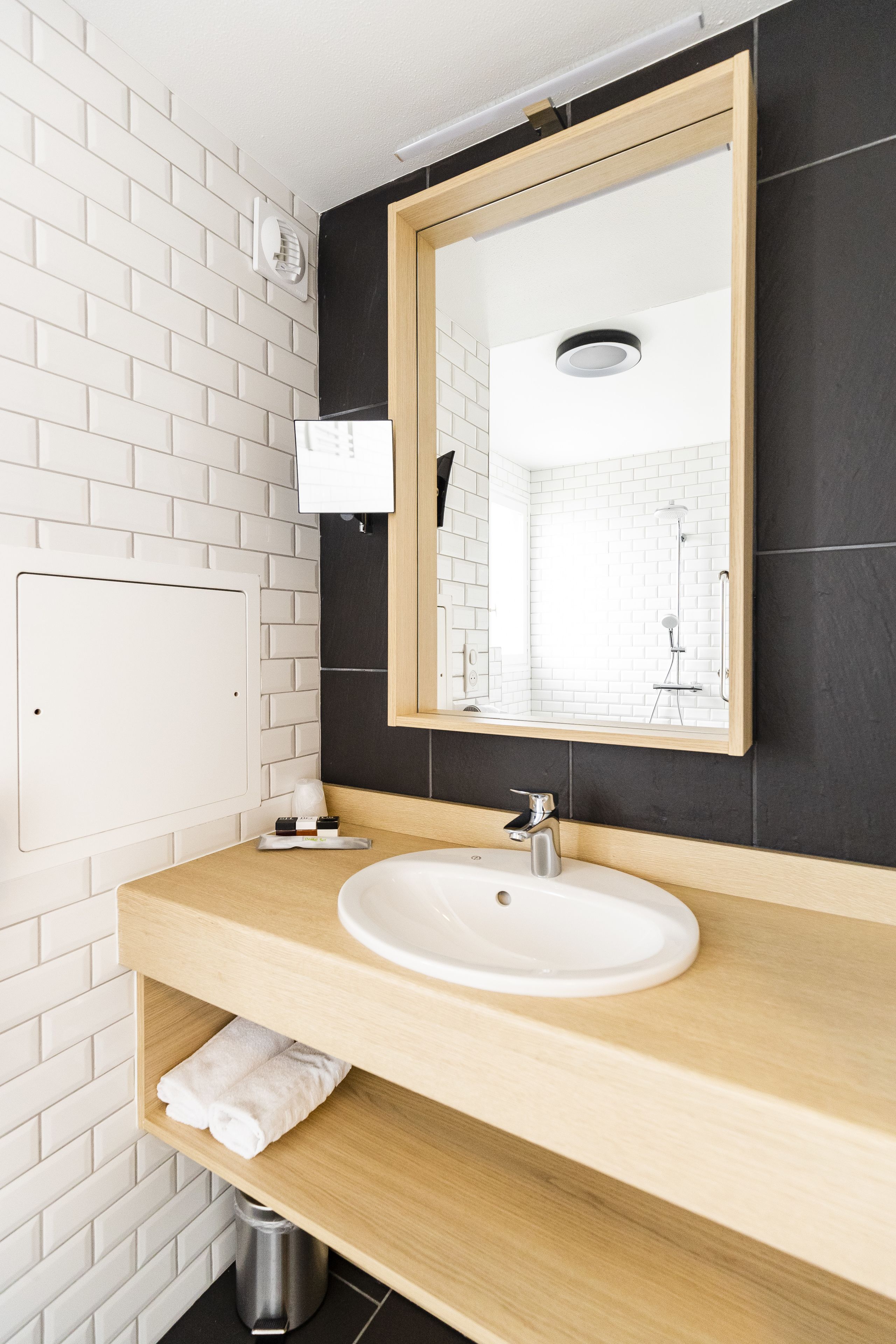A modern bathroom with a white sink, wooden vanity, and a large mirror.