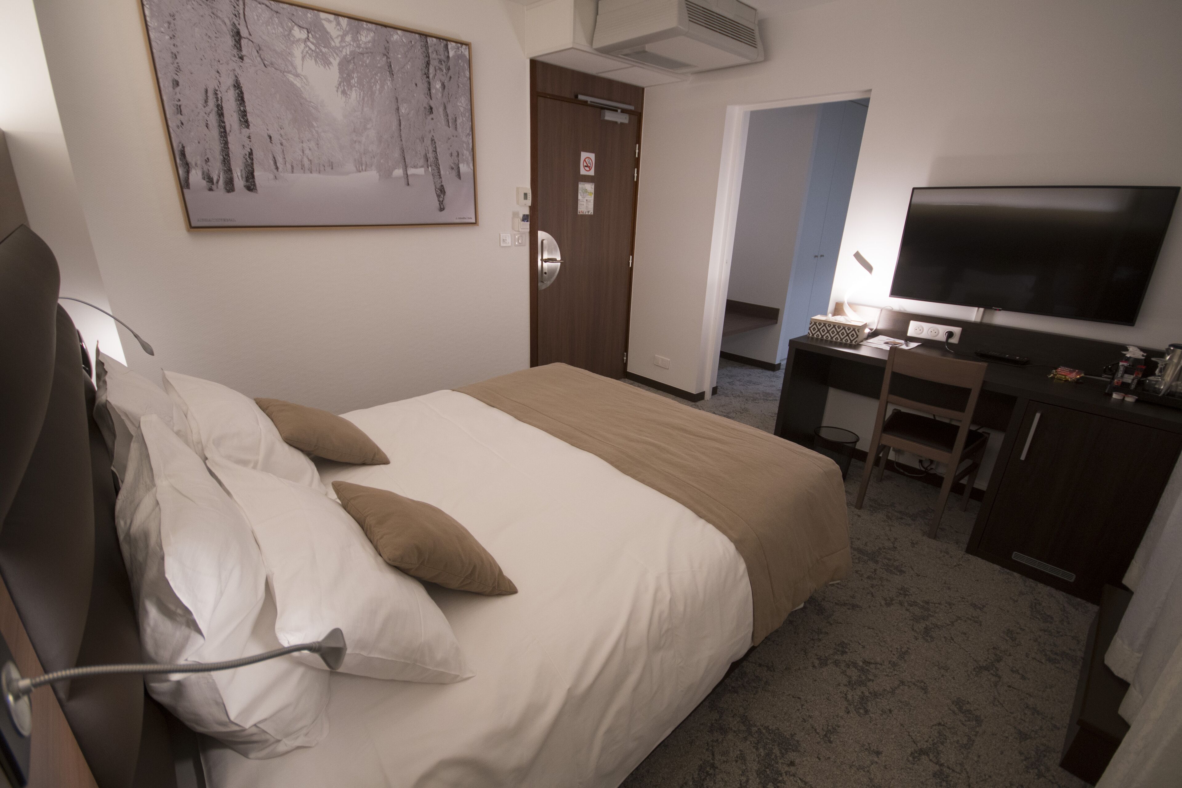 A hotel room with a bed, a desk, a television, and a door.