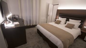 Habitación de hotel con cama, mesitas de noche, un escritorio con lámpara, televisor y puerta.