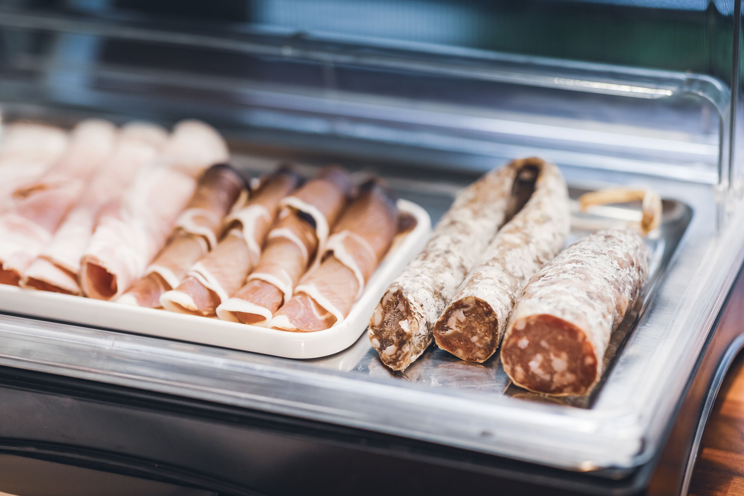 Una vitrina con diversos tipos de embutidos curados, como salchichas enrolladas y salami en rodajas.