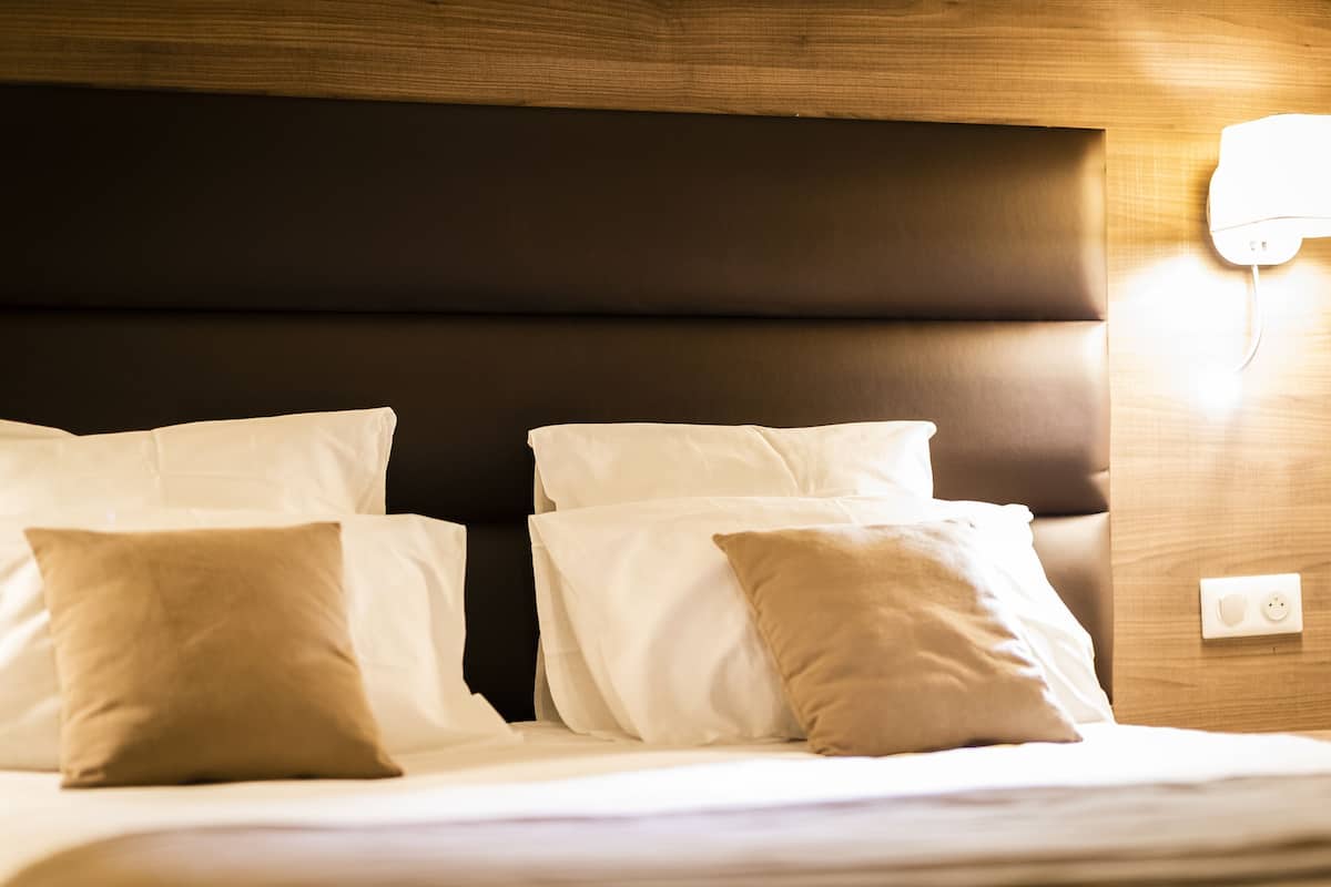 A bed with white and beige pillows, a wooden headboard, and a wall socket.