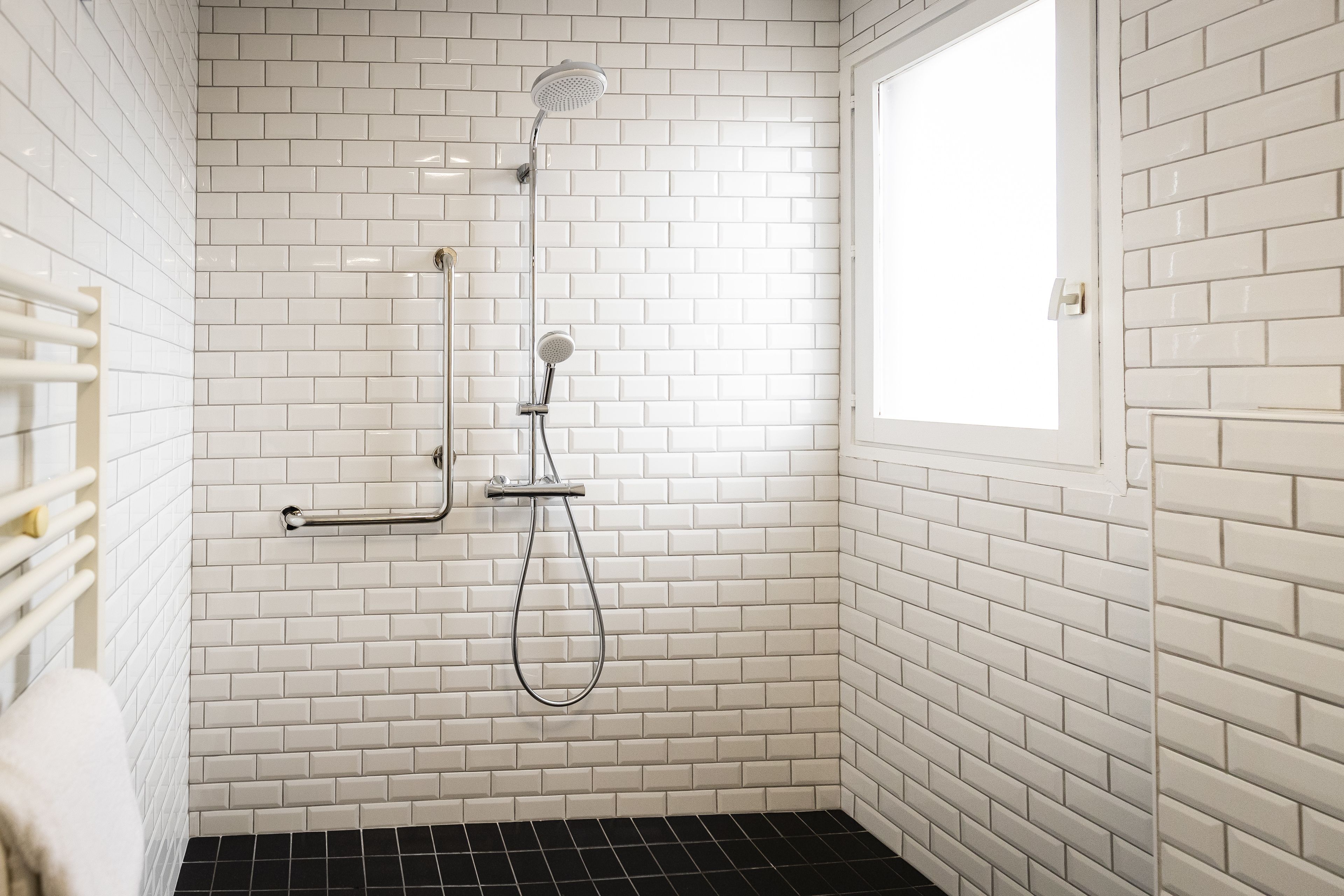 Un baño con azulejos blancos tipo metro, ducha con cabezal de ducha manual y ventana.