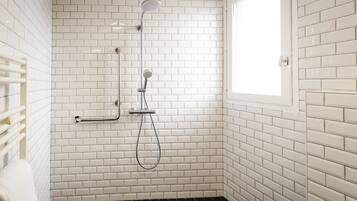 Un baño con azulejos blancos tipo metro, ducha con cabezal de ducha manual y ventana.