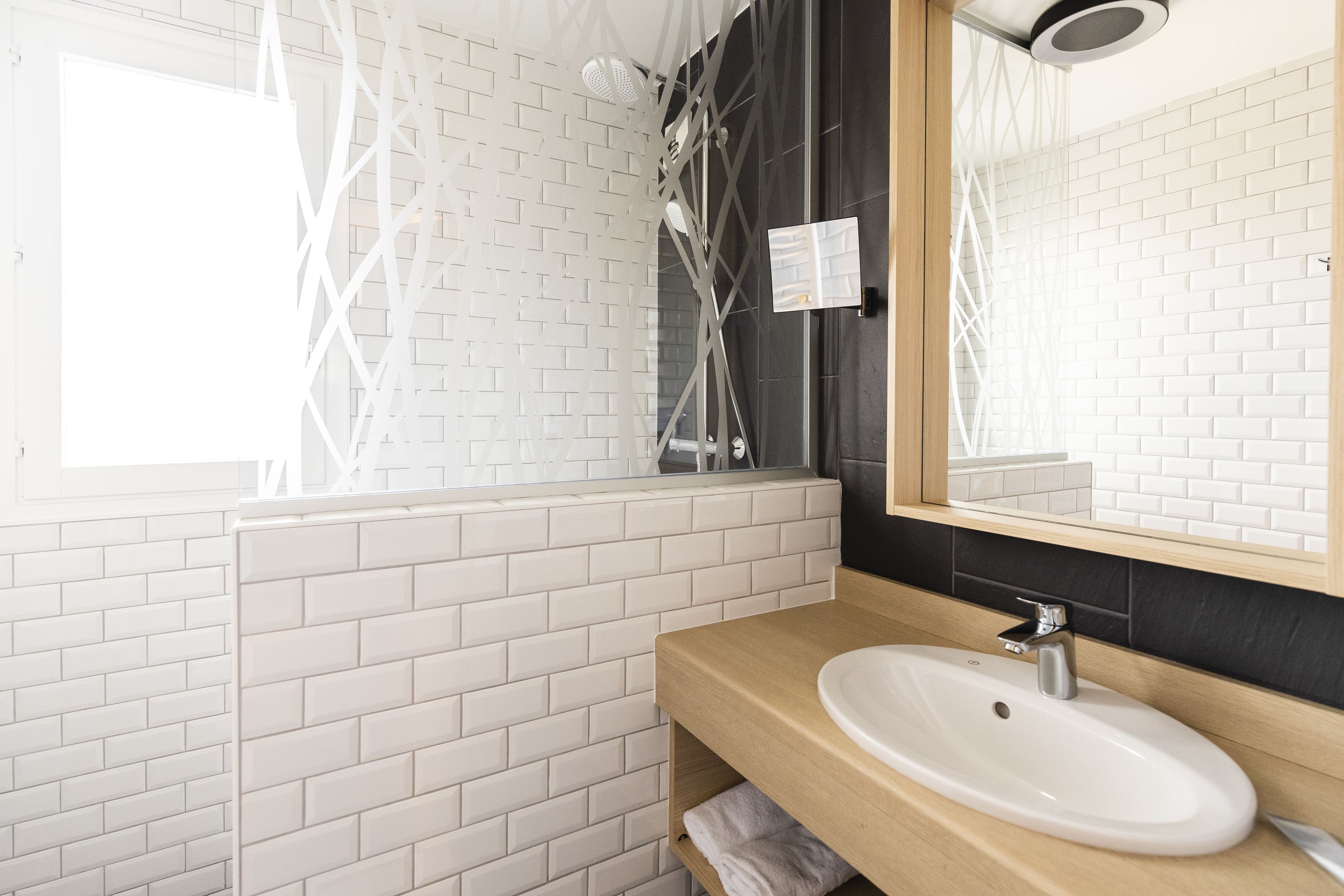 A bathroom with a white brick wall, a wooden vanity with a sink, and a large mirror.