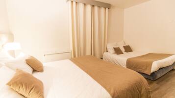 Una habitación de hotel con dos camas, ropa de cama color beige, una ventana con cortinas y suelo de madera.