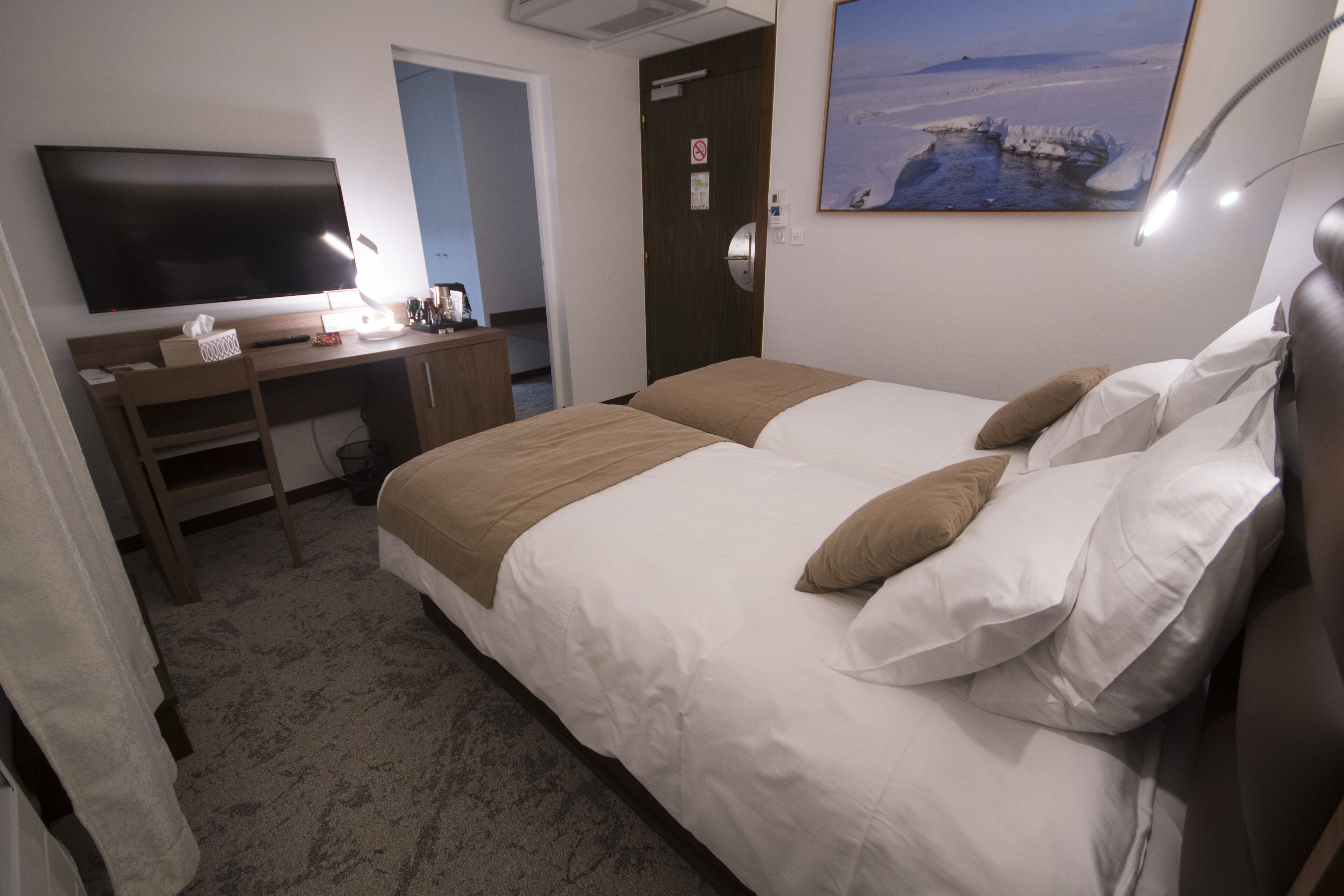 A hotel room with a bed, a desk with a computer, a TV, and a painting on the wall.