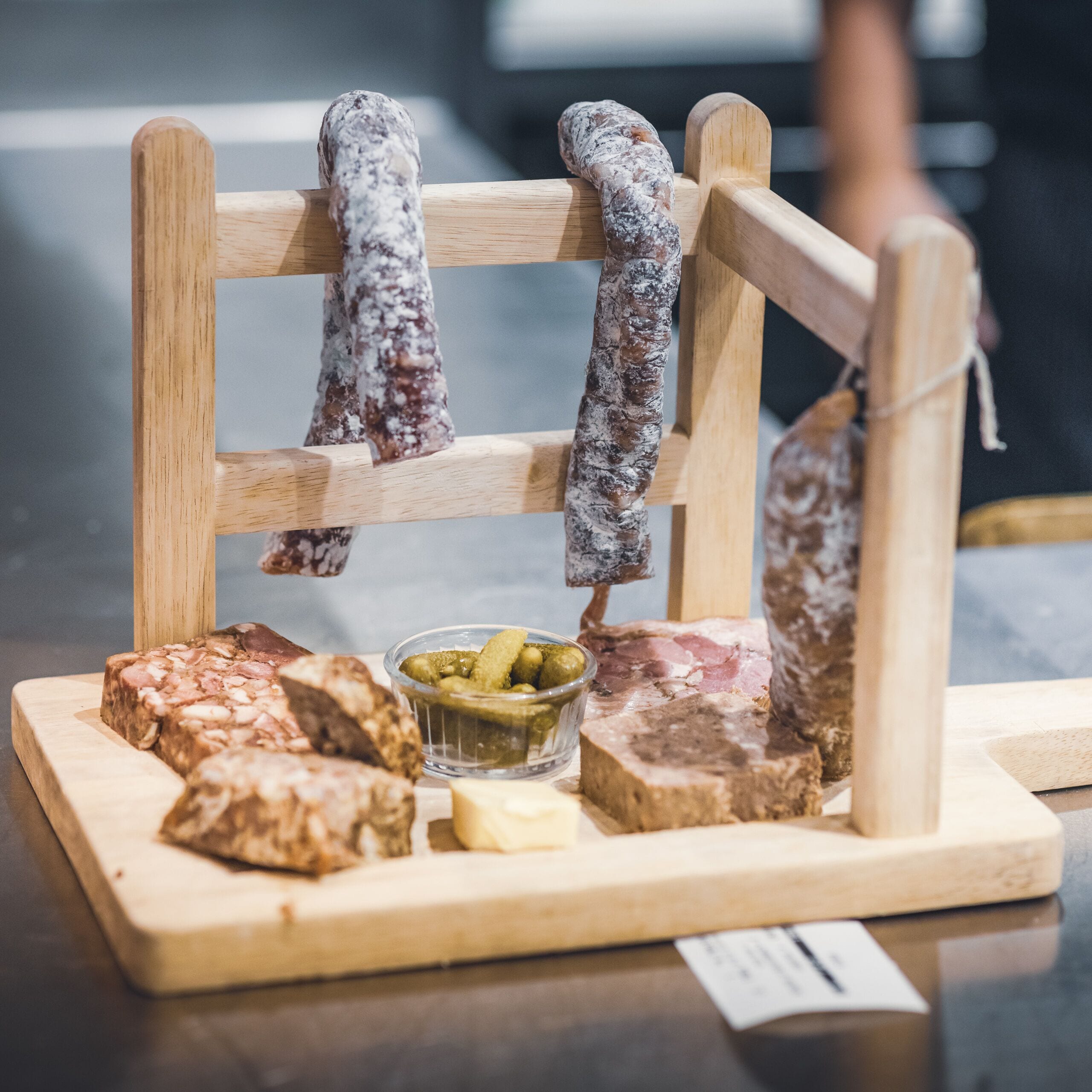 A wooden board with various cured meats and a small bowl of pickles.