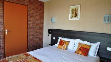 A hotel room with a brick wall, a bed with patterned bedding, and artwork on the walls.