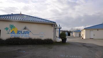 A hotel named AZUR HOTEL with a signboard, a parking area, and a building with a blue roof.