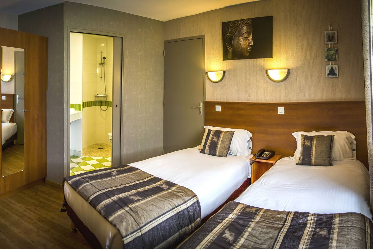 A hotel room with two beds, a shower area, and a wooden headboard.