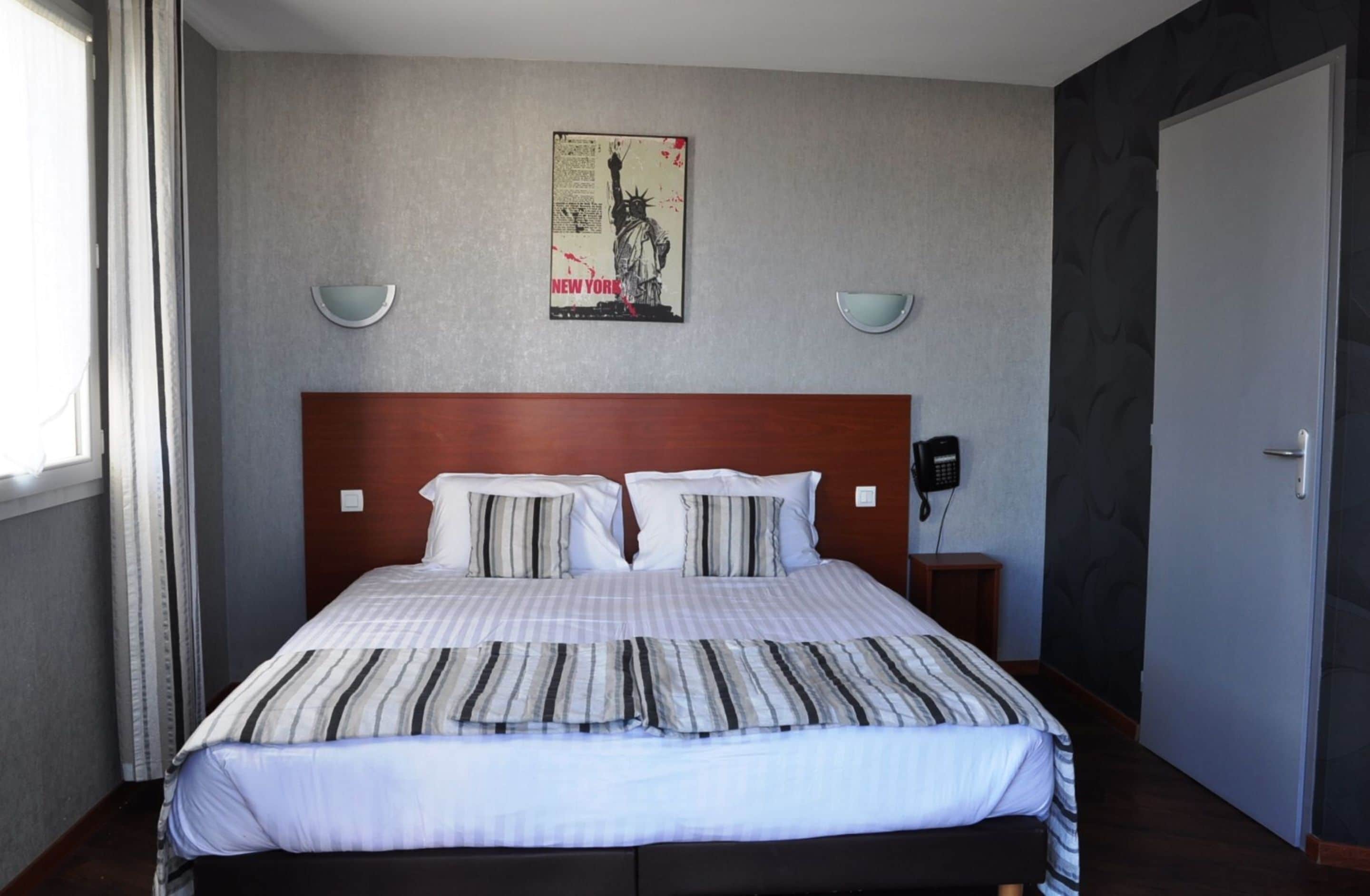 Una cama bien hecha con ropa de cama a rayas, un cabecero de madera y una obra de arte en la pared que representa la Estatua de la Libertad.