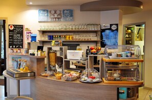 Una barra de desayuno con diversos alimentos, una máquina de café y cristalería en estantes.