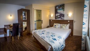 Habitación de hotel con cama, escritorio, silla, armario y zona de ducha.