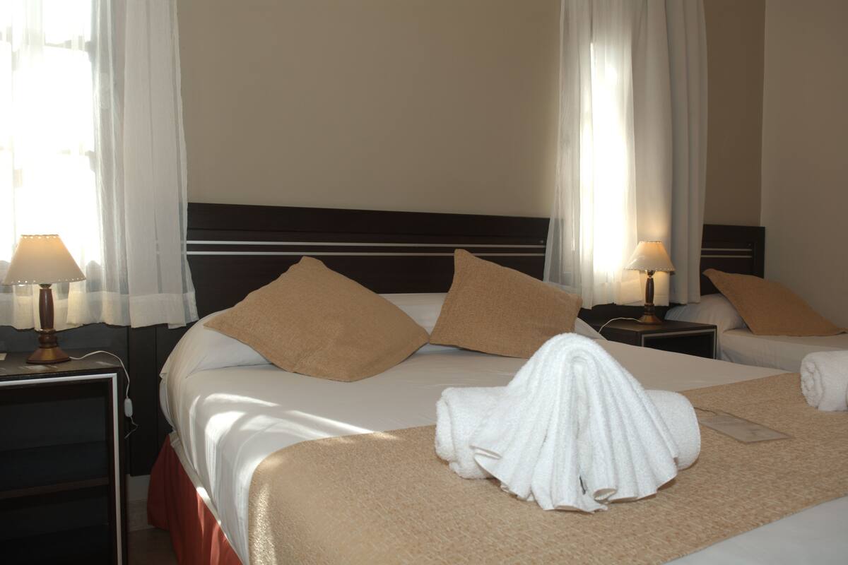 A hotel room with a large bed, two nightstands, a lamp on each, and a window with sheer curtains.