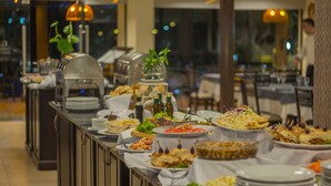 Una barra de buffet con diferentes platos, entre ellos ensaladas, pasta y postres, dispuesta sobre una mesa larga.