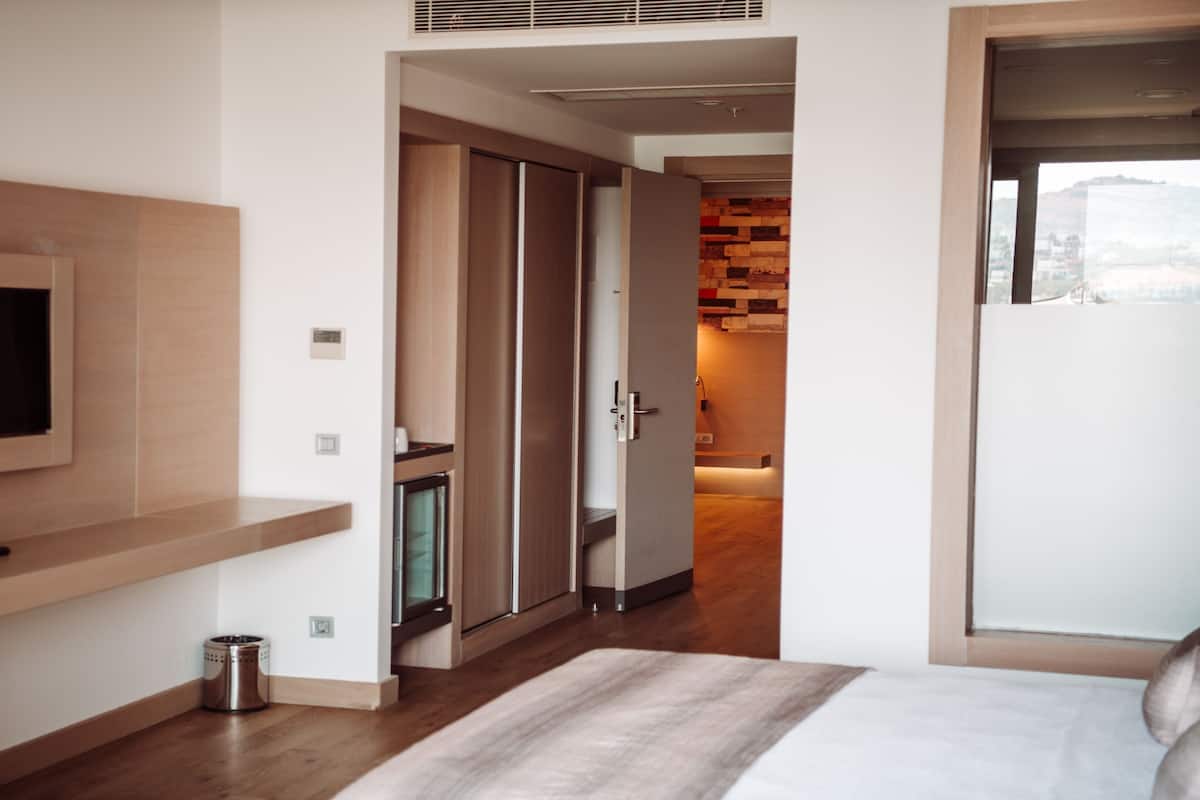 A modern bedroom with a TV mounted on the wall, a bed with a white and grey striped blanket, and wooden flooring.