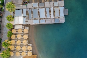 An aerial view of a beachside resort with multiple sun loungers and umbrellas, a wooden deck, and a clear view of the ocean. - Costa Farilya Special Class Hotel Bodrum - Special Class (Bodrum)