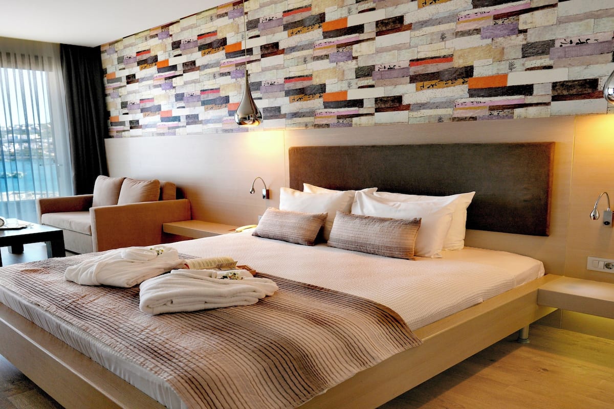 A modern hotel room with a large bed, a sitting area, and a view of the sea.