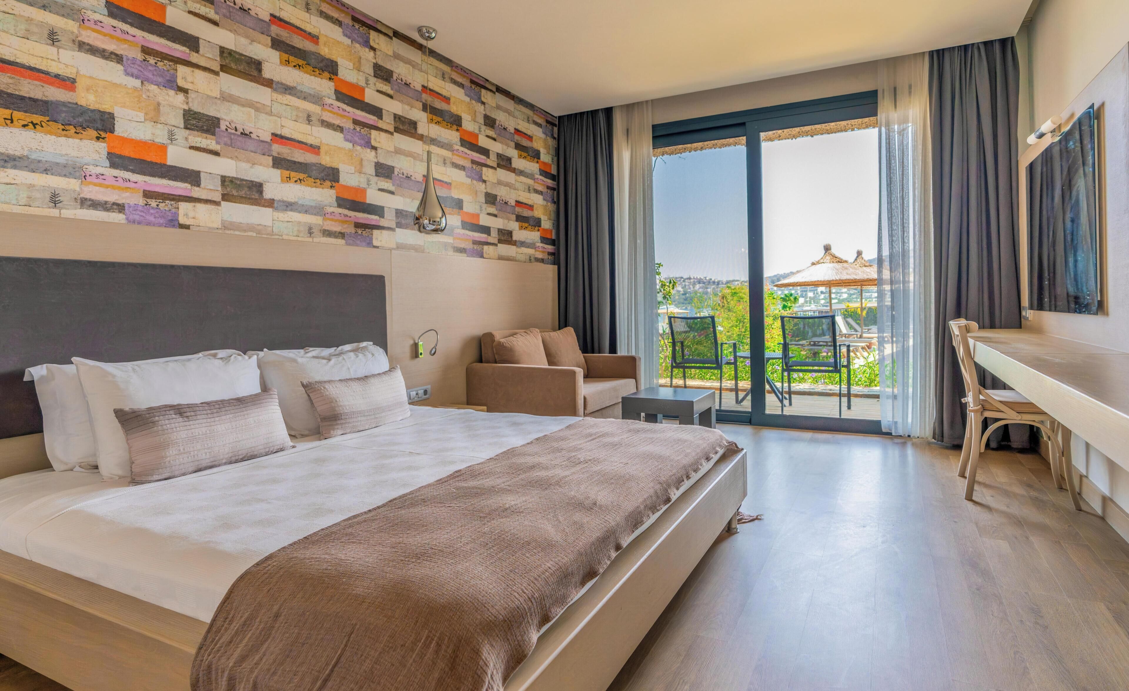 A hotel room with a large bed, a sofa, a desk, and a balcony with a view.