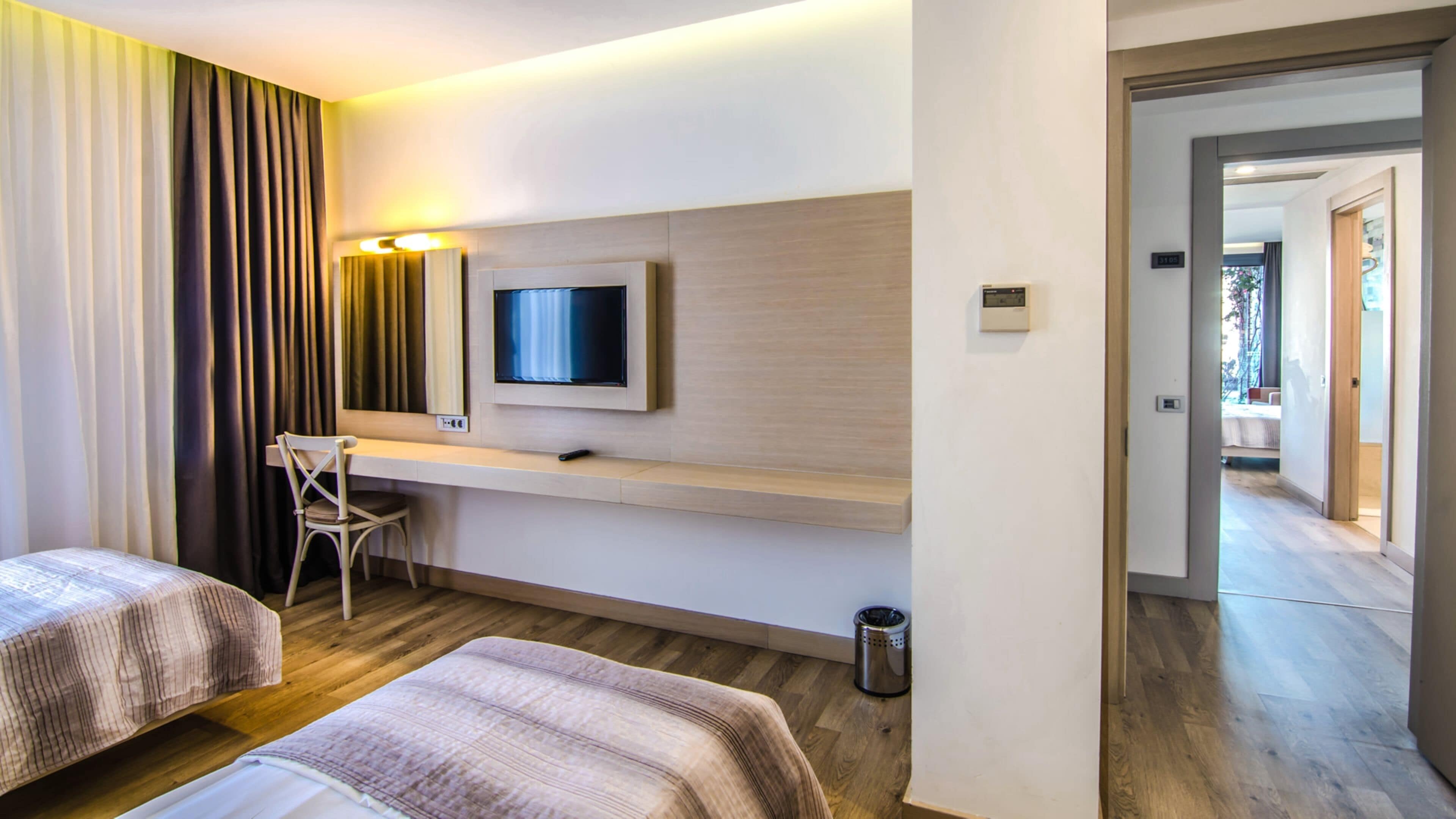 A hotel room with two beds, a desk, a television, and a view of the outside.