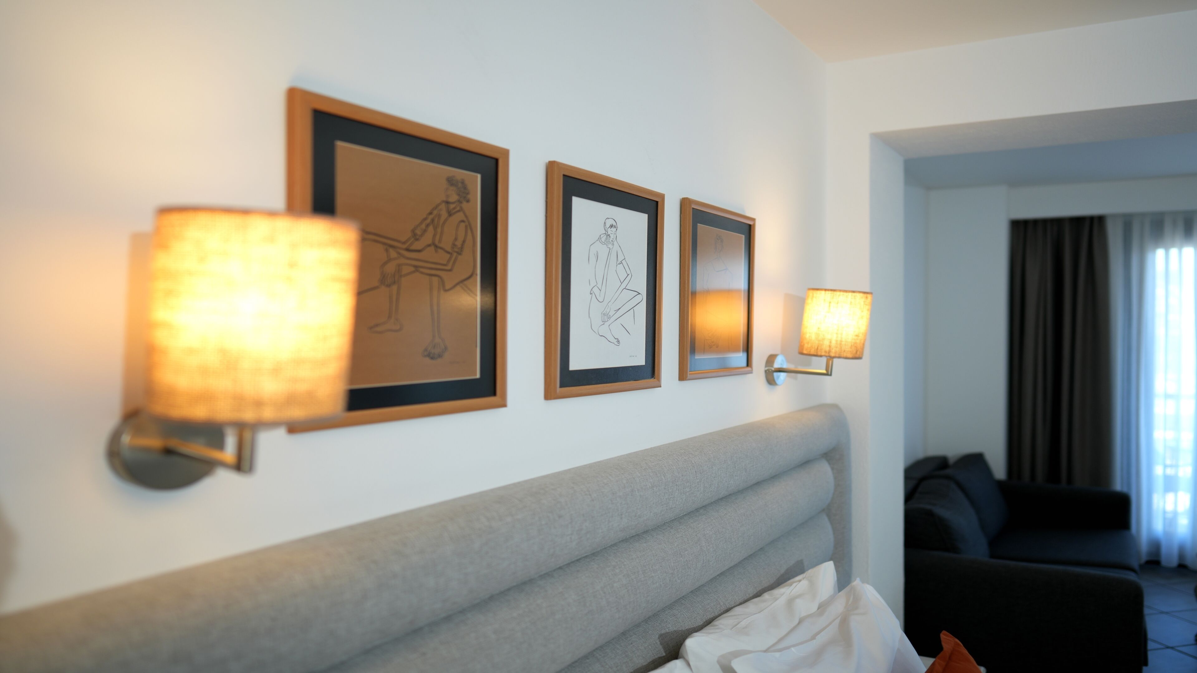 Quarto de hotel com cama, cabeceira e luminárias fixadas na parede.