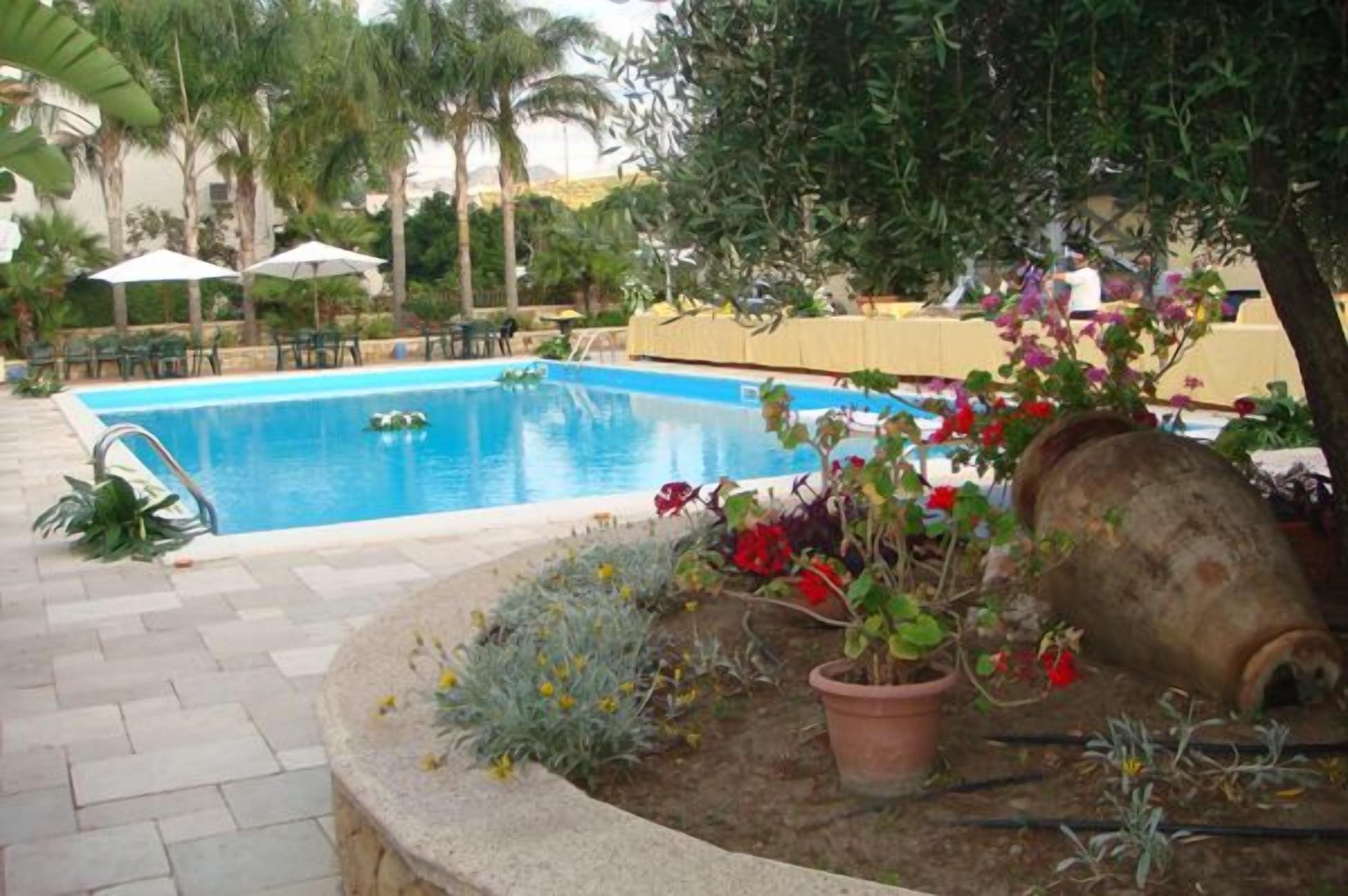 A swimming pool with a tiled deck, surrounded by potted plants and outdoor furniture.