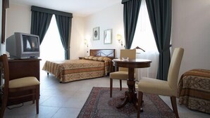 Una habitación de hotel con una cama, una silla, una mesita, un televisor y dos ventanas con cortinas.