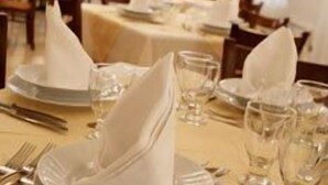 Una mesa de comedor dispuesta con servilletas blancas dobladas en forma triangular, cristalería transparente y cubertería.