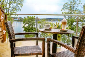 Un conjunto de silla y mesa de mimbre en un balcón con vista a un lago y árboles.