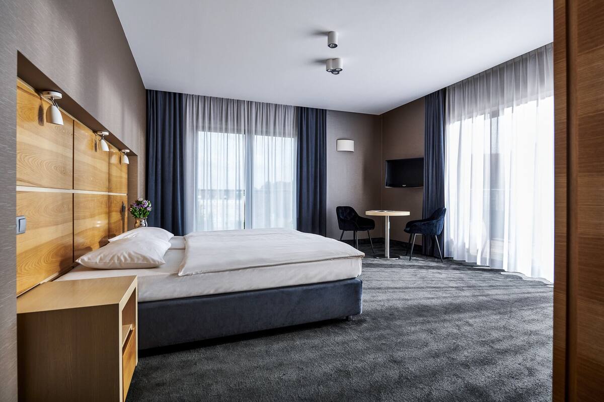 A modern hotel room with a large bed, a wooden wardrobe, a desk, and a TV.