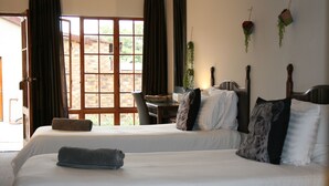 A hotel room with two beds, a desk, and a view of a brick building through a large window. - Aero Guest Lodge (Kempton Park)