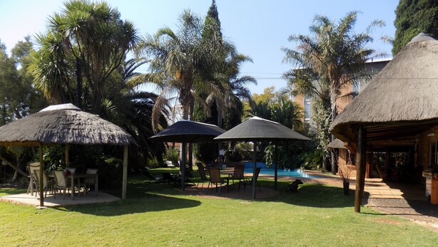 A courtyard with thatched-roof structures, a pool, and lush greenery. - Aero Guest Lodge (Kempton Park)